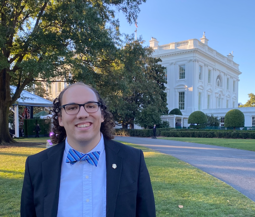 Isaac F. Weiss stands in front of the White House wearing a dark suit and blue bow tie.